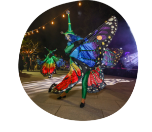 Two dancers, one in the background, dressed and dancing as butterflies with market lights hanging